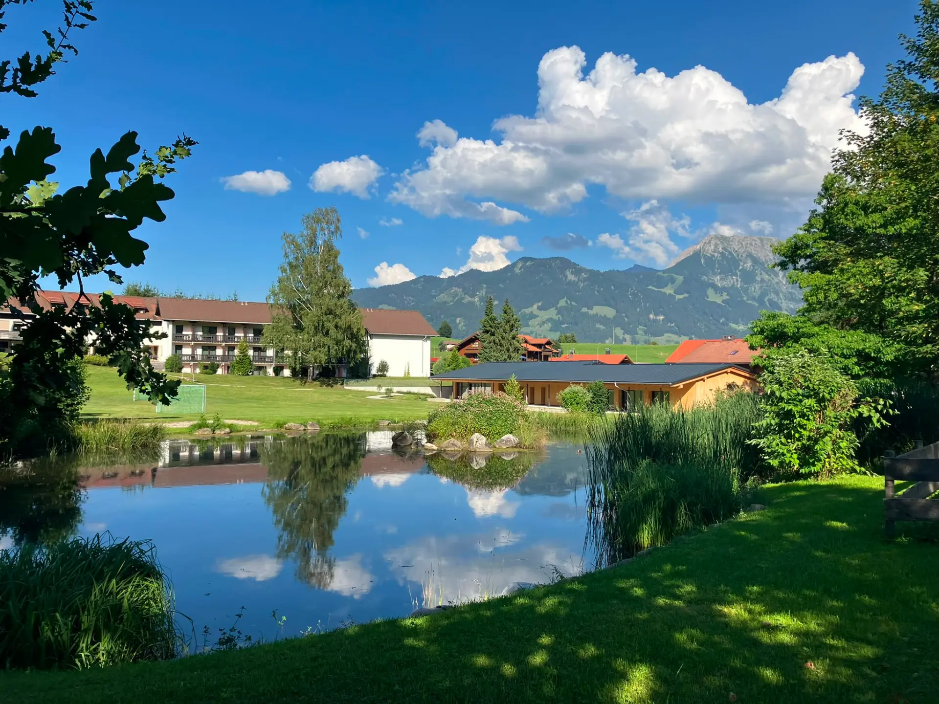 See mit Spiegelung von Wolken und Bergen, umgeben von Wiesen und Häusern